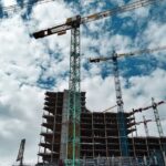 Urban construction site with numerous cranes framing rising skyscrapers against a blue sky.