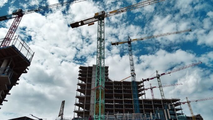 Urban construction site with numerous cranes framing rising skyscrapers against a blue sky.